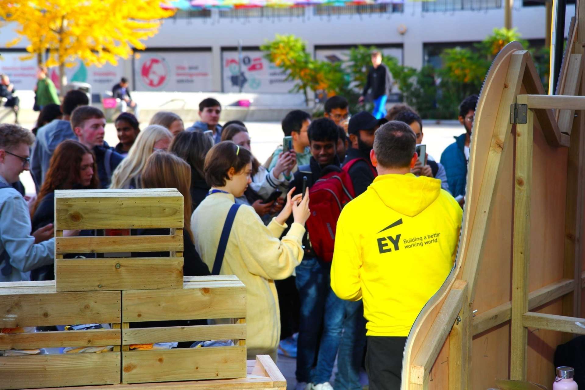 A group of University of Liverpool students attending a career fair, engaging with an EY representative in a bright outdoor setting.