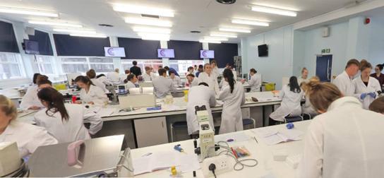 A group of individuals in white lab coats engaged in a discussion within a lab setting.