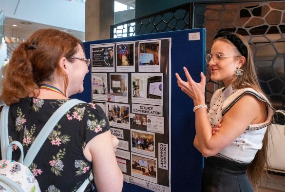 Ieva Andrulyte discussing her public engagement work with a female showcase attendee, standing in front of Ieva\'s poster
