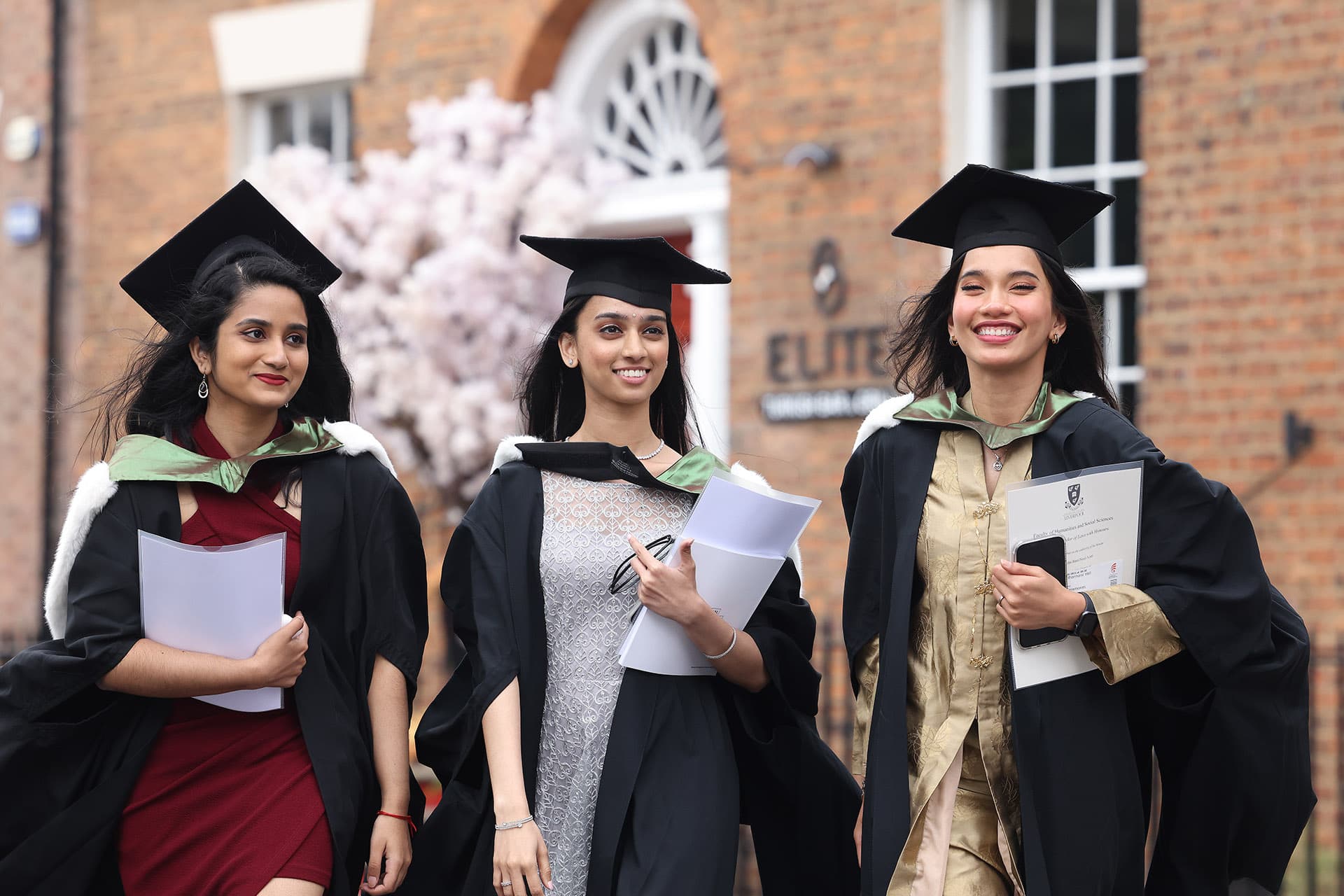 Three female students dressed for graduation holding their degree certificates