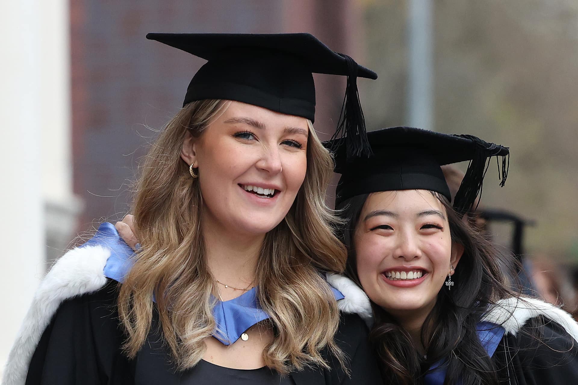 Two students dressed in cap and gowns smiling. They have just graduated.