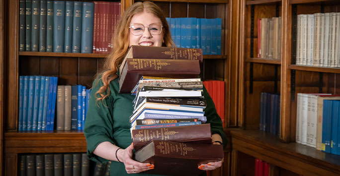student carrying a stack of books from the library