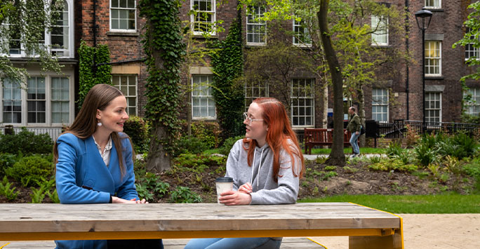 two students sat on bench smiling and talking