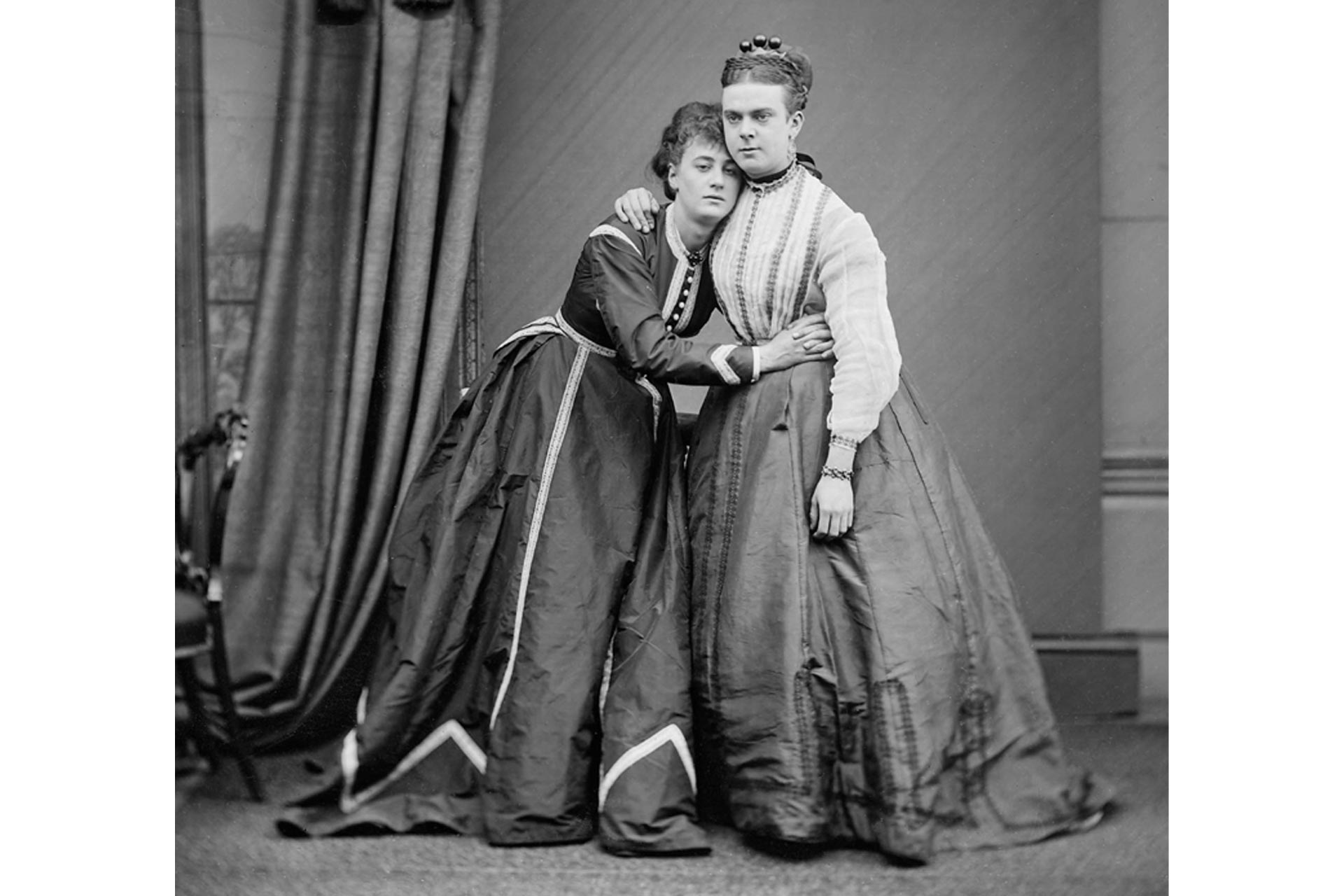 Black and white full length image of two people in the Victorian era wearing long dresses