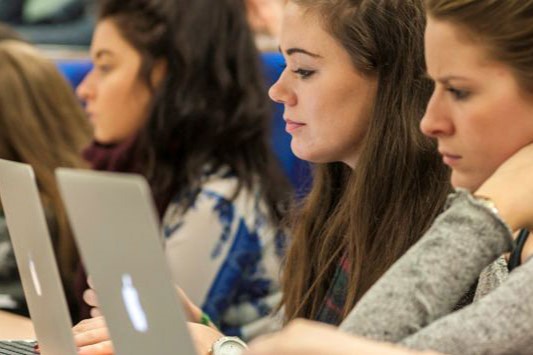 Students  sat in a lecture, taking notes on laptops