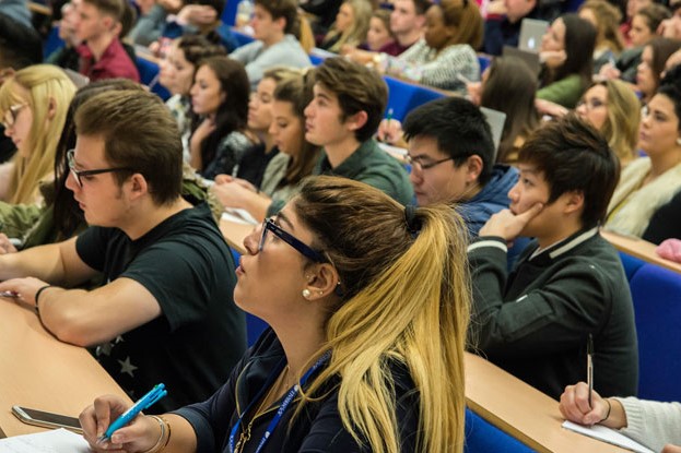 An image of multiple students in a lecture theatre looking at a screen which is out of frame