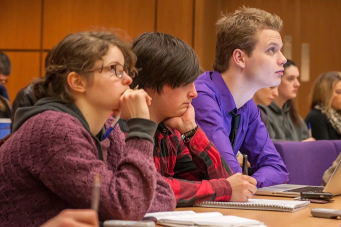 Multiple students sat at a desk looking at something out of frame