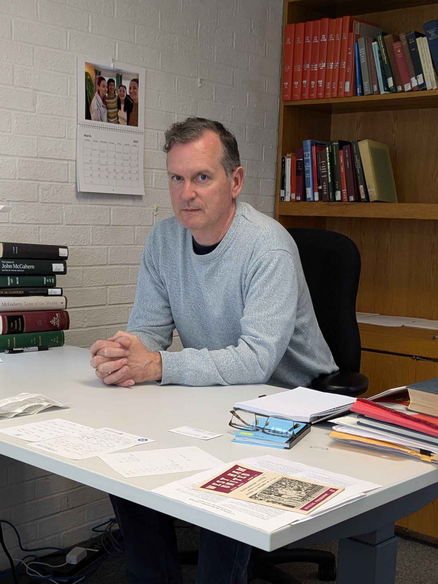 Prof Frank Shovlin at his desk in his study space at NHC. Books and papers are on his desk, and more books are on the shelves behind him.