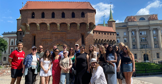 A group of students stand together in front of a large brown building in Krakow.