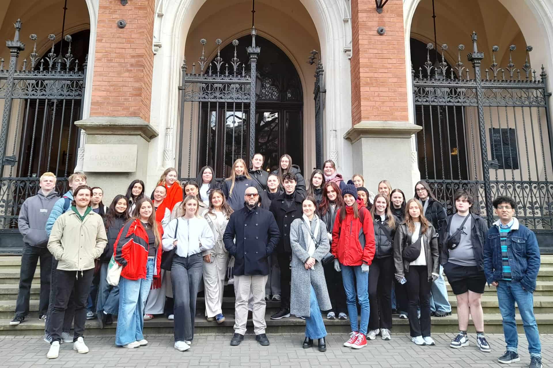 A large group of student posing together outside of a large grand building.