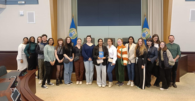 A group of students stand together inside of the Organisation for the Prohibition of Chemical Weapons building.