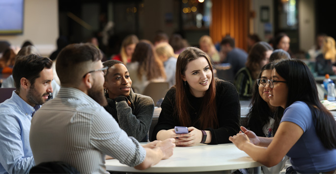 A group of students sat around a table in conversation with each other.