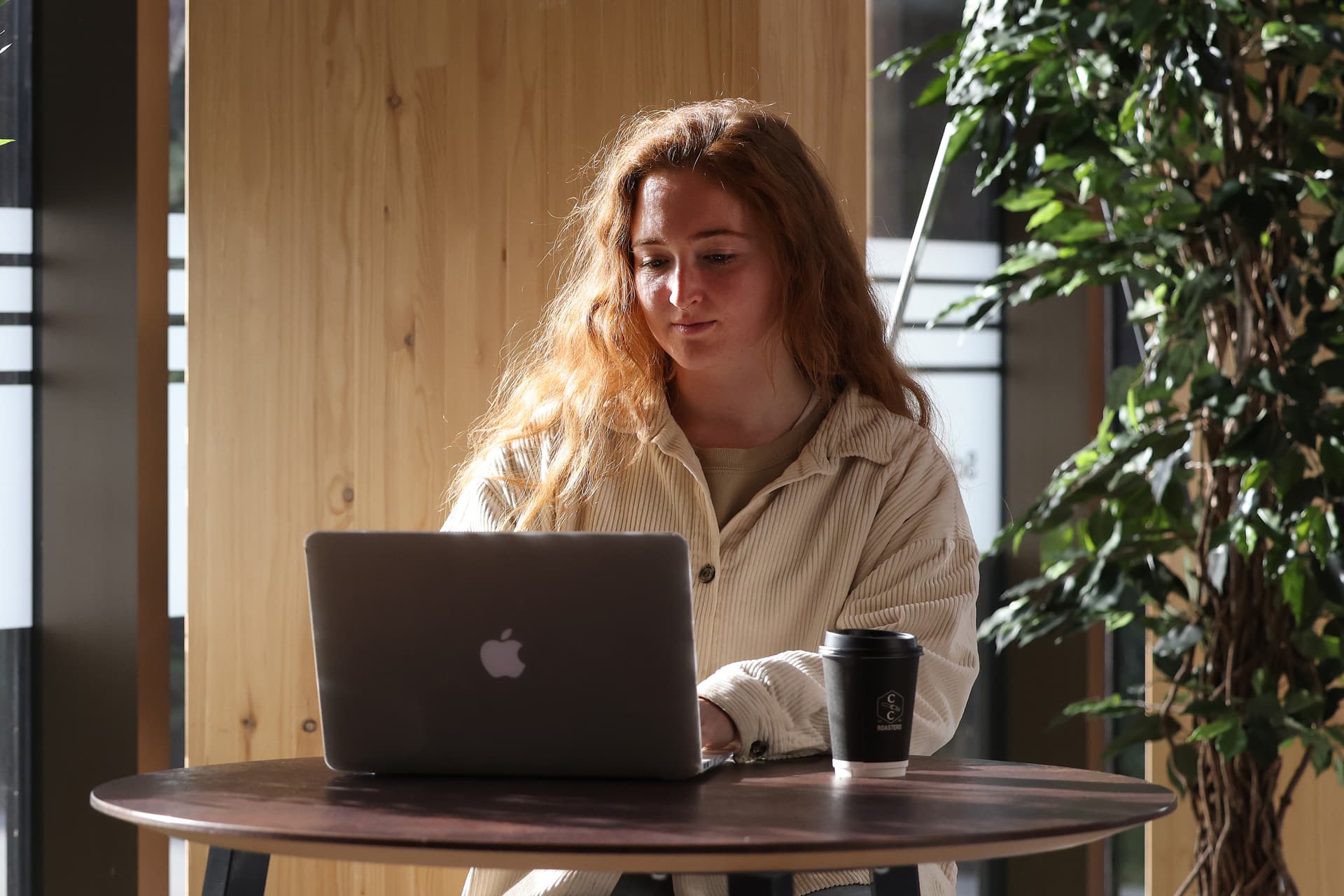 A students sits at a table working on a laptop.
