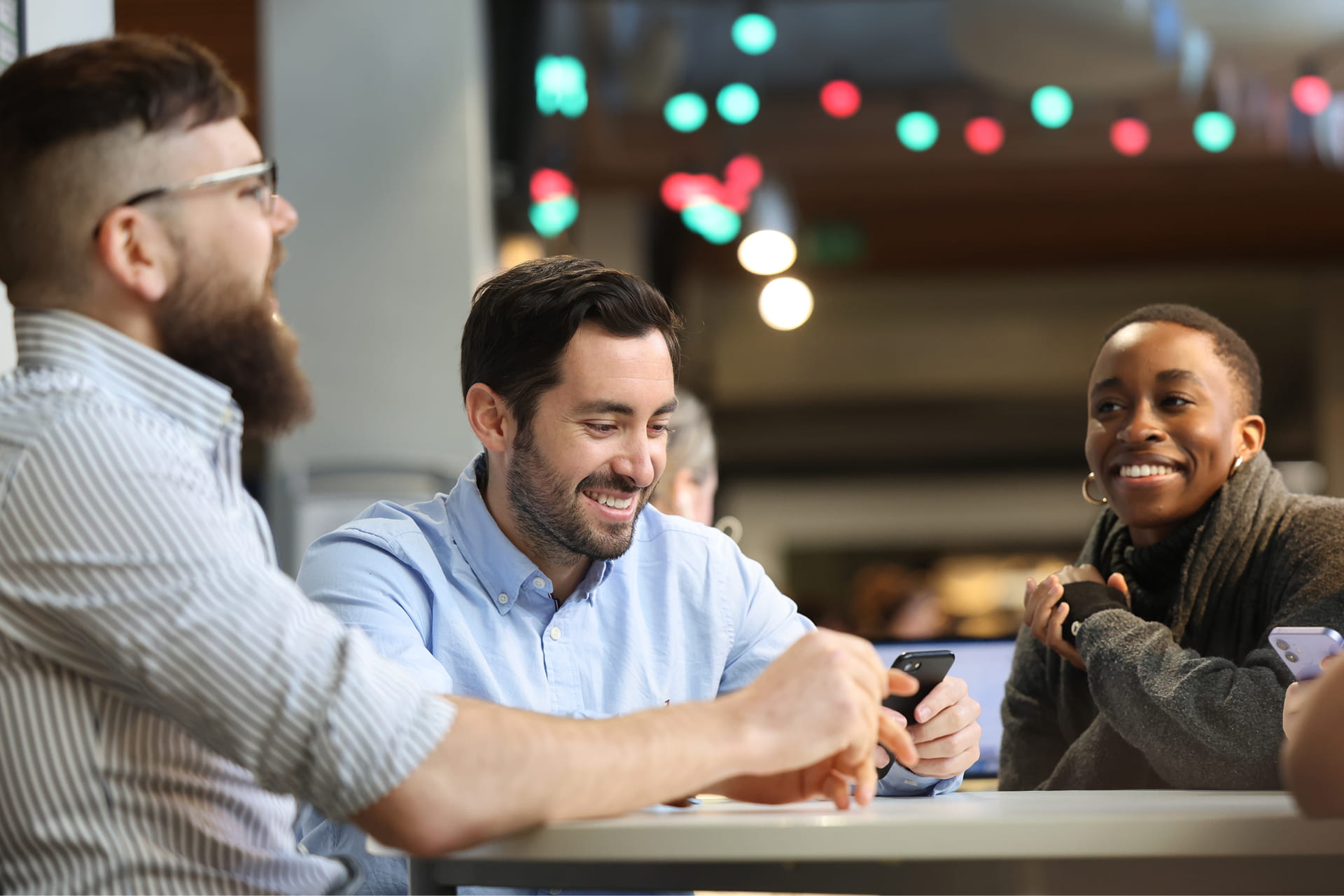 Three students sit around a table together, engaged in conversation with eachother.