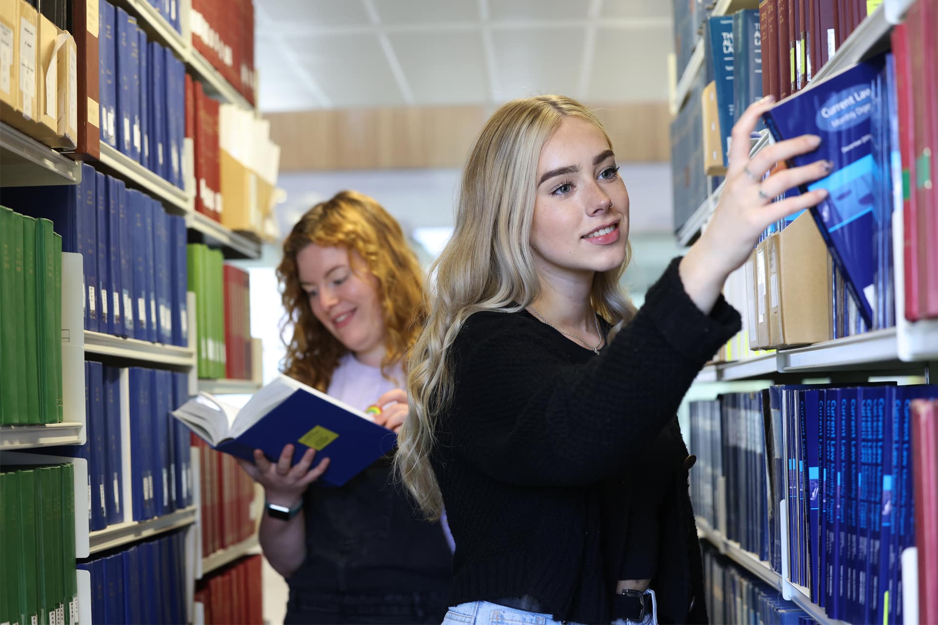 Two students stand between tall shelves filled with legal books, browsing the collection.