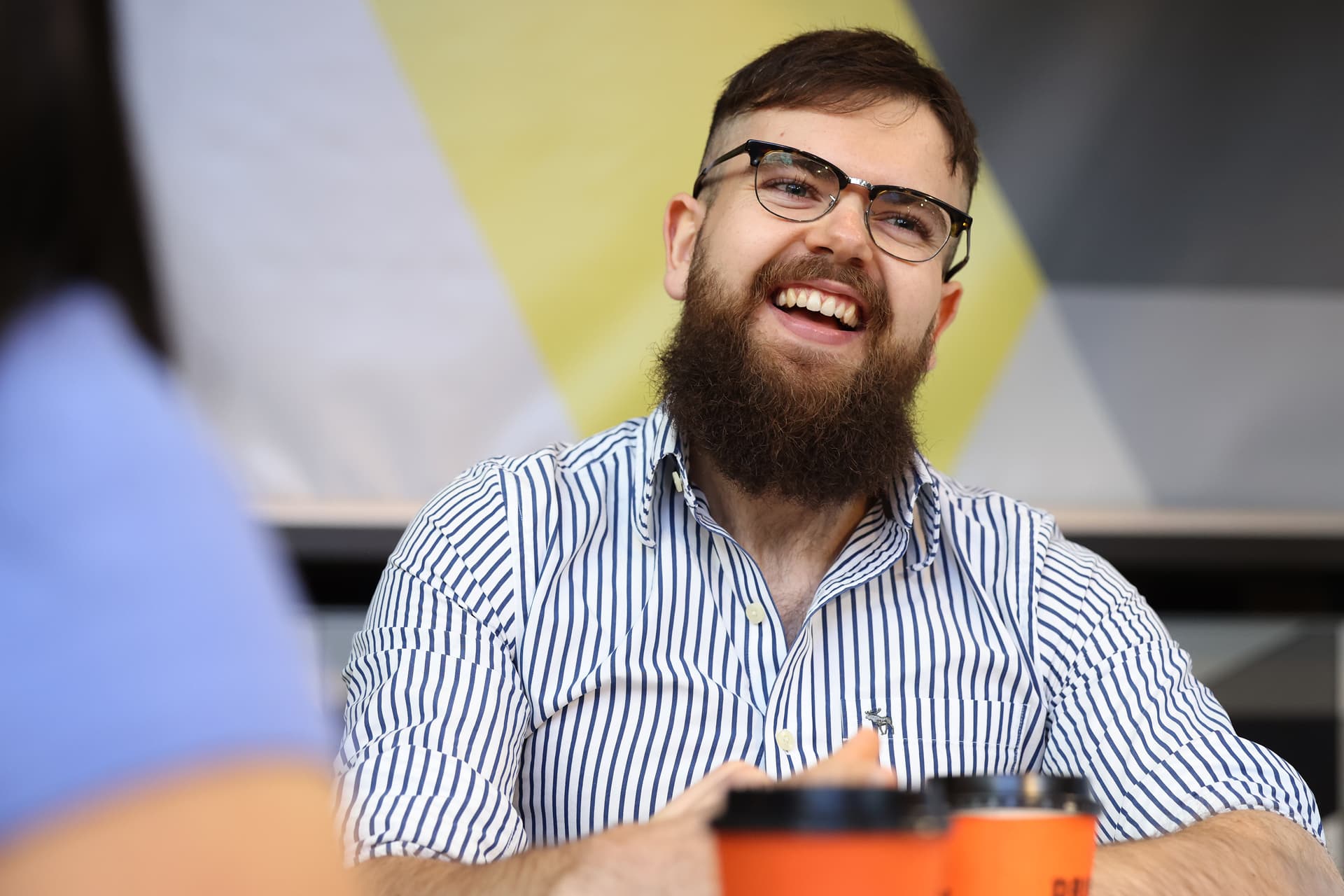 A student sits at a table, smiling while looking off-camera.