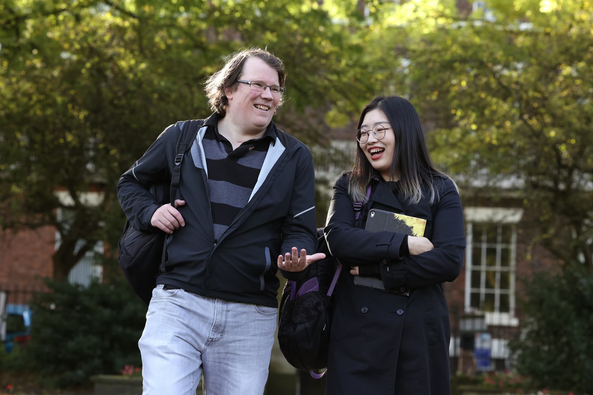 Two students walk together through a leafy campus.
