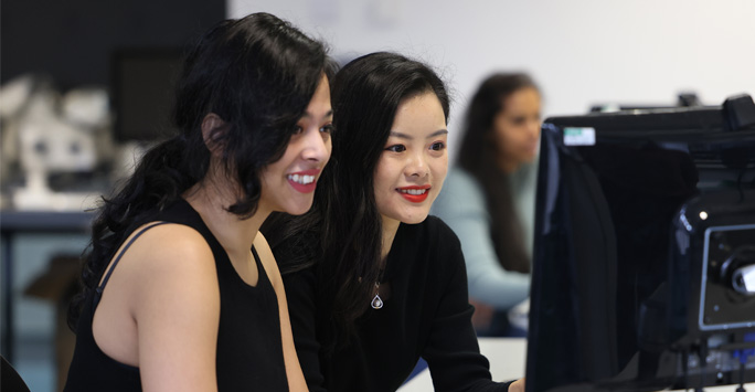 Two students sit together and look at a computer screen.