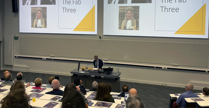 A lecture filled with people. At the front of the room is Mr Justice Foxton, with a large screens behind him, giving a talk.
