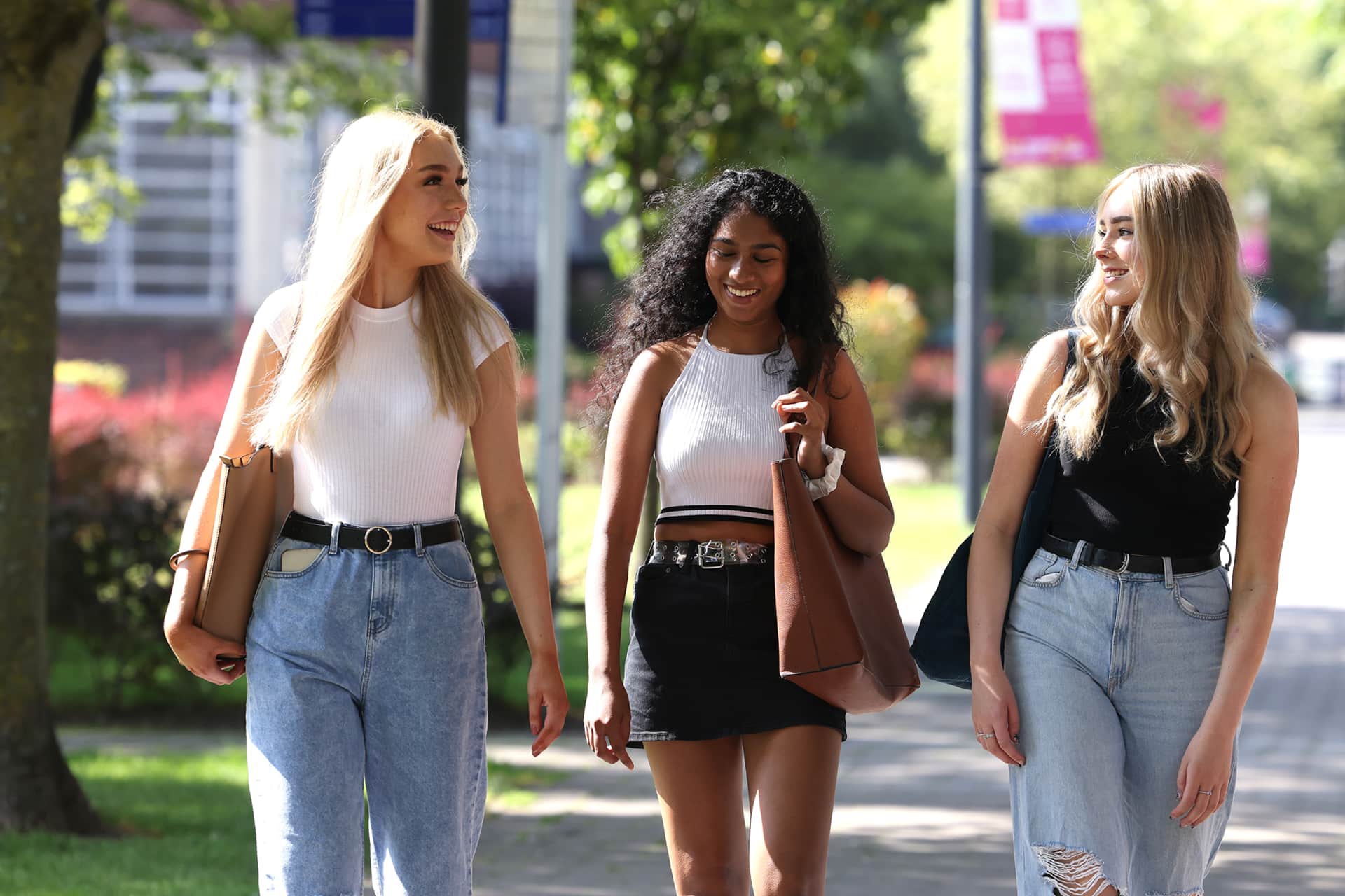 Three students walk through campus together on a sunny day.