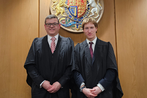 Two students stand together dressed in barristers cloaks.