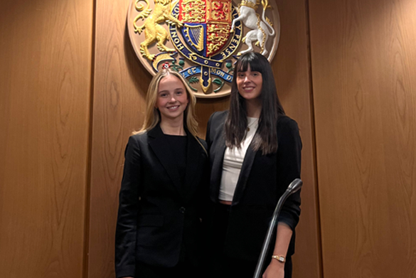 Two students stand together dressed in barristers cloaks.