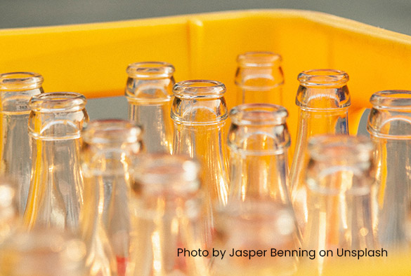 Empty glass bottles in a yellow crate. Credit reads \'Photo by Jasper Benning on Unsplash\'
