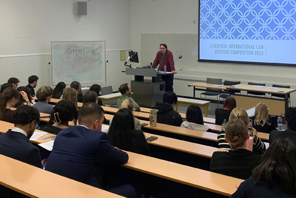 A lecture theatre filled with attendees, with a speaker presenting at the front.