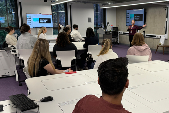 A large group of student sit at desks in the Liverpool Law Clinic computer suite looking at the speaker at the front of the room.