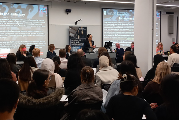 A judge stands at the front of a large room, addressing a room full of students.