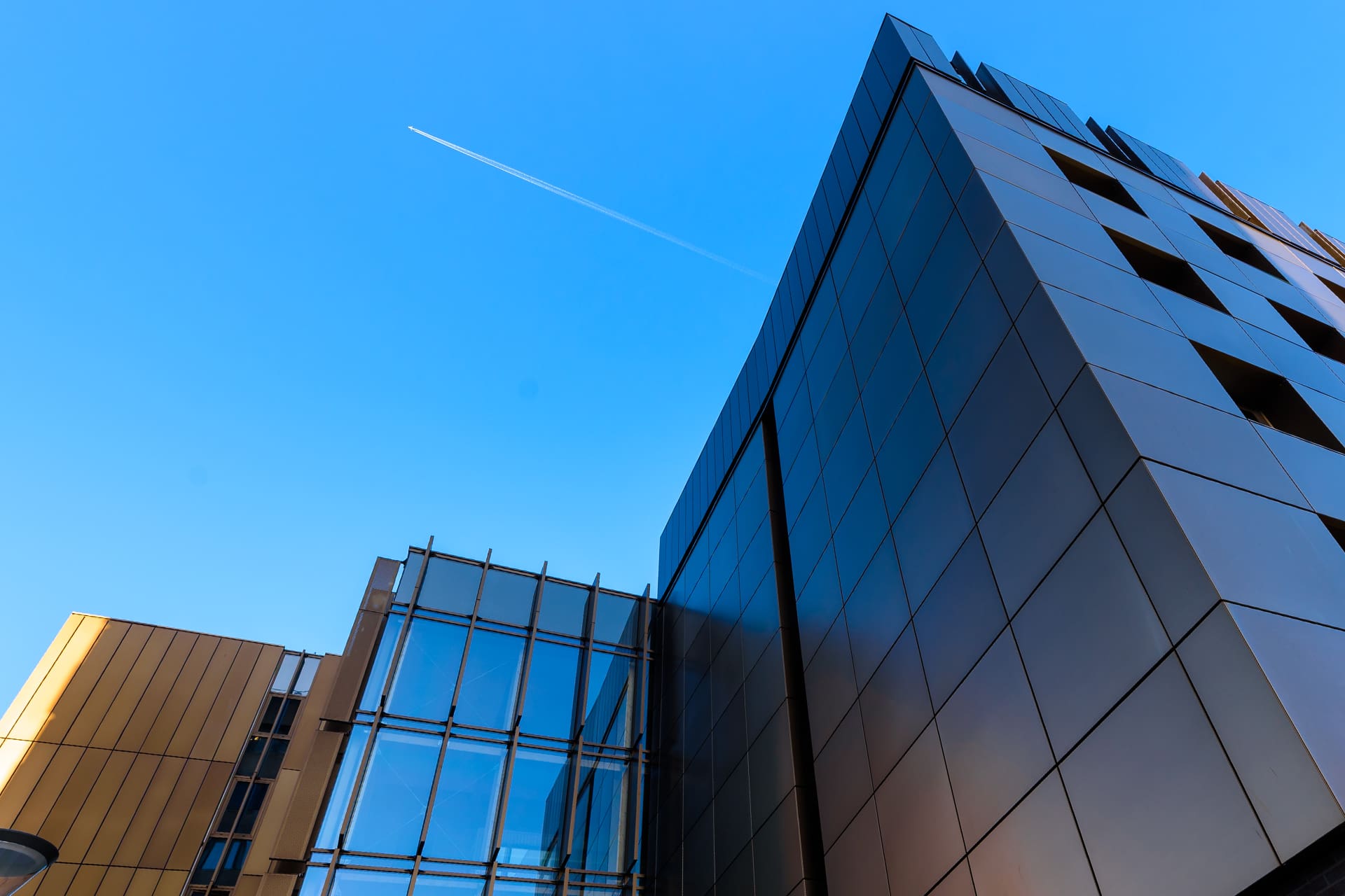 A building stands below a plane flying overhead against a clear blue sky.