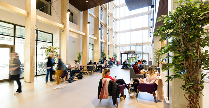 The foyer of the School of Law and Justice, featuring a spacious, open area with a large window at one end. Students and staff are seated on chairs and sofas.