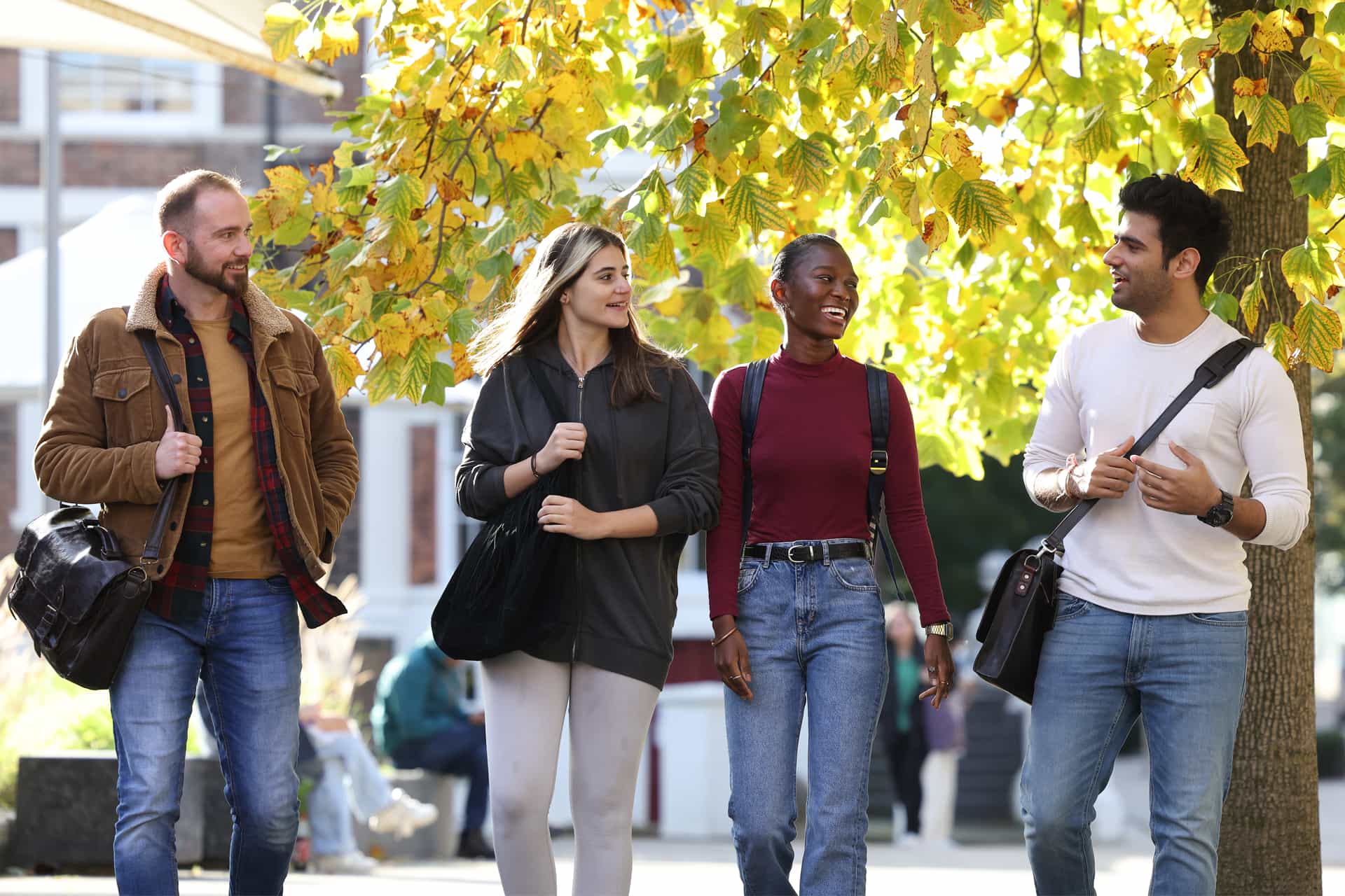 Four students walk alongside each other through campus.
