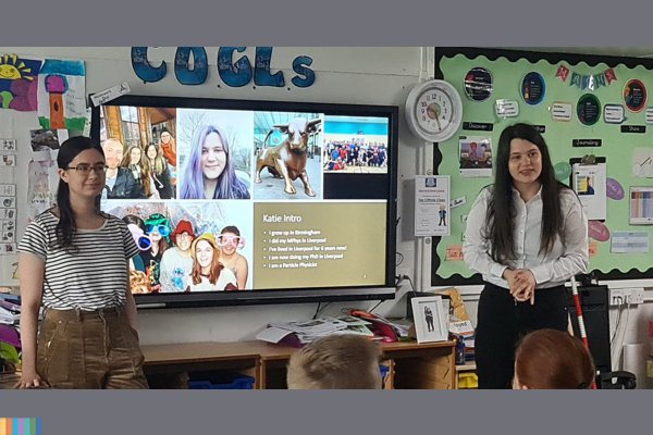 Two students talking to school children in a class room.