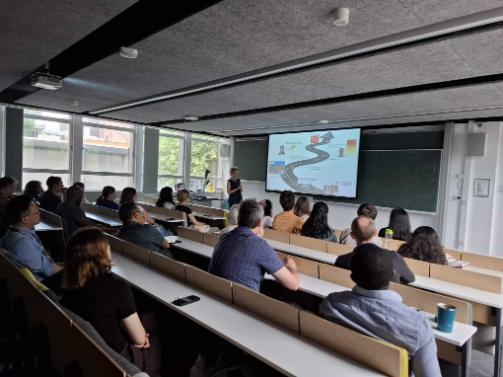 A group of people seated in a classroom, focused on a presentation displayed on a projector screen.