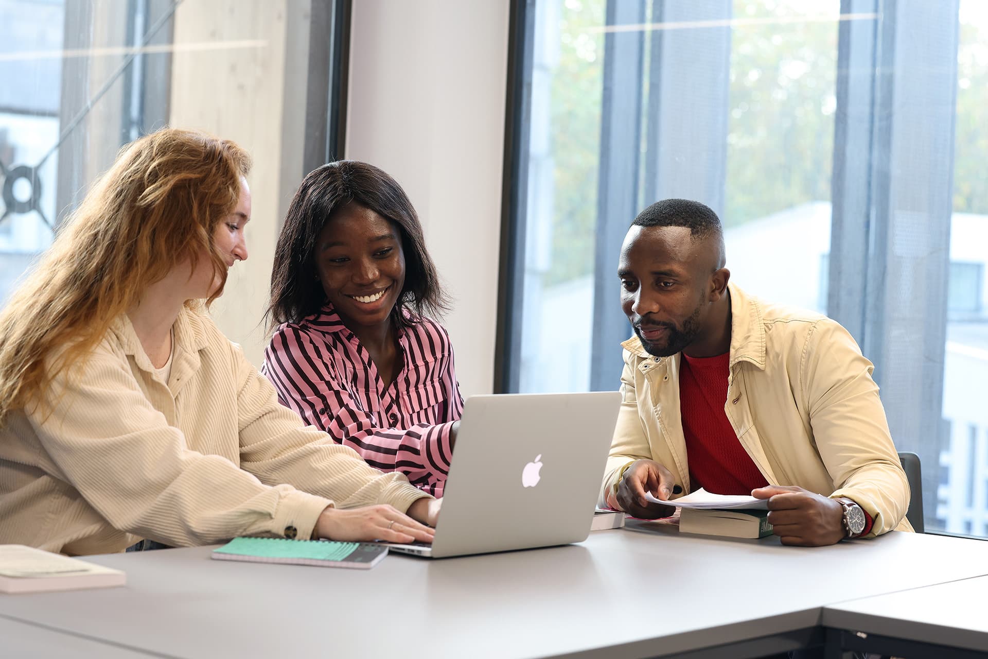 Three students sitting at a table looking at a laptop and chatting