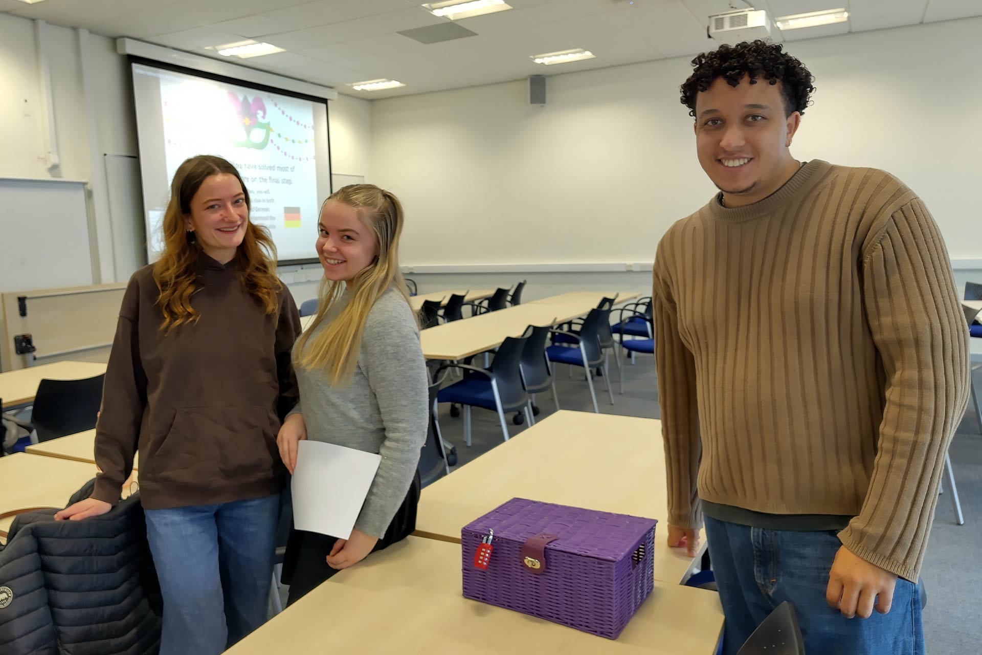 Three students in a teaching room standing and smiling at the camera