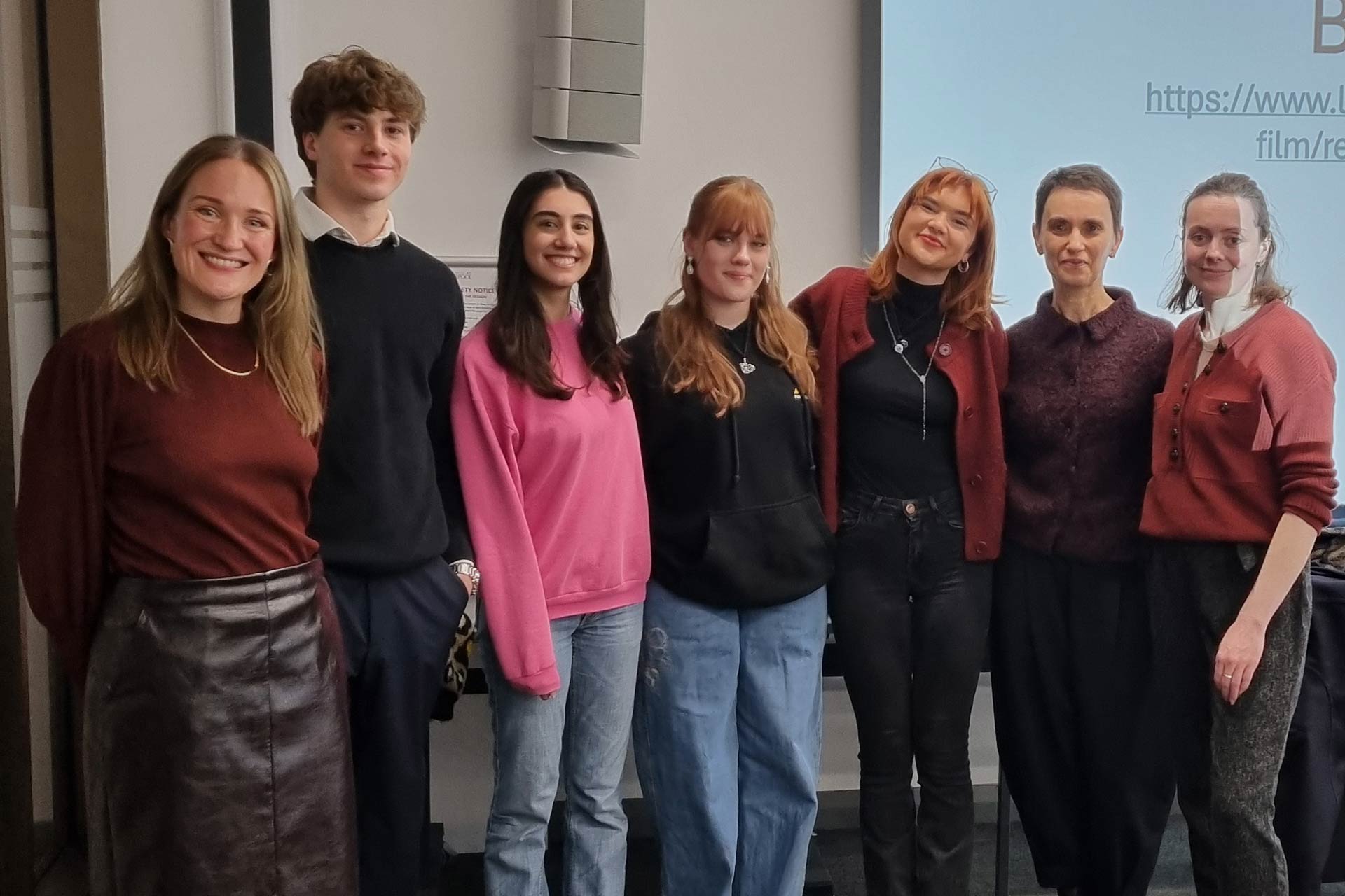 6 women and one man standing in a row and smiling at the camera