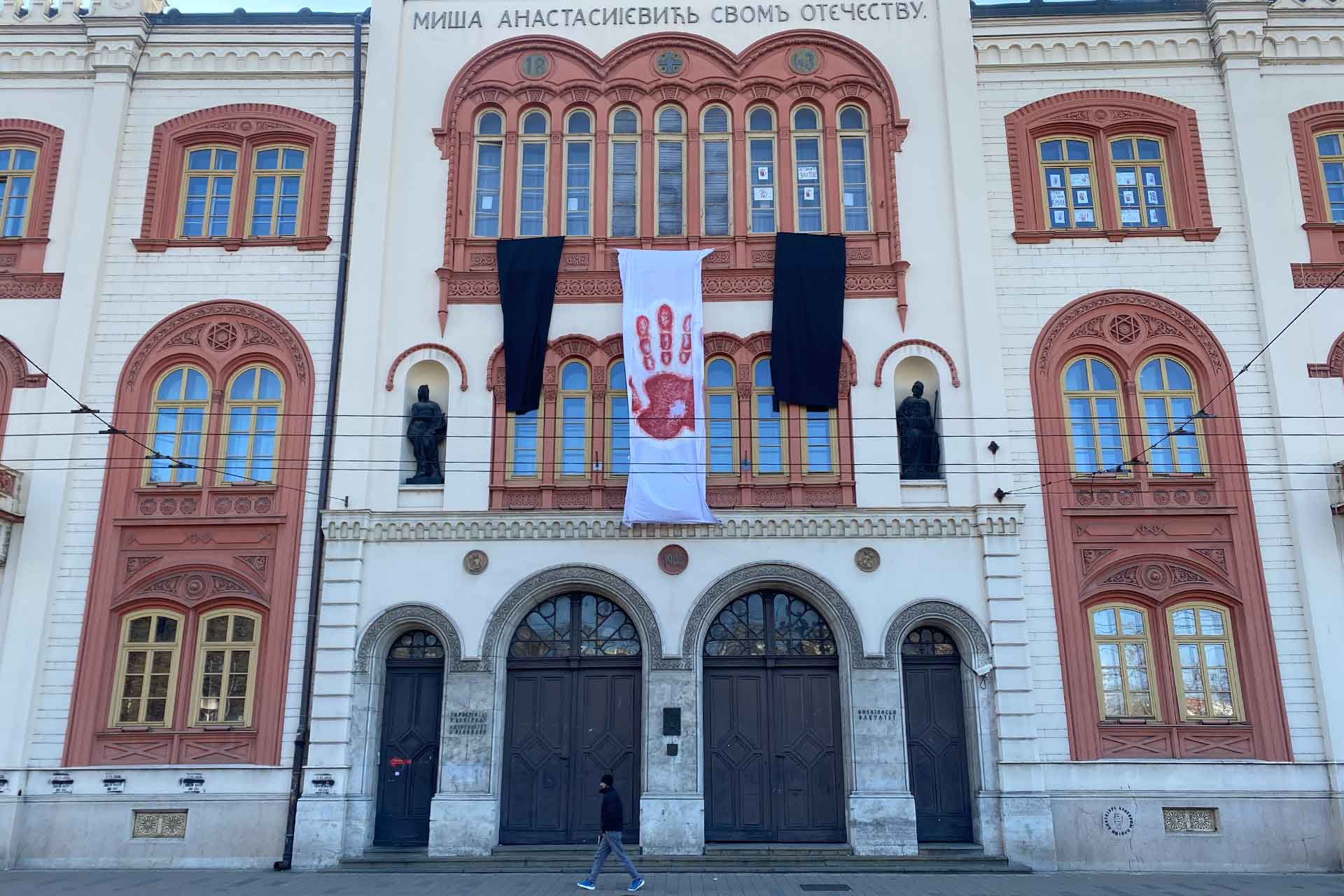 A building with a large white flag with a red handprint in the centre and two black flags at the side, attached to the front of the building