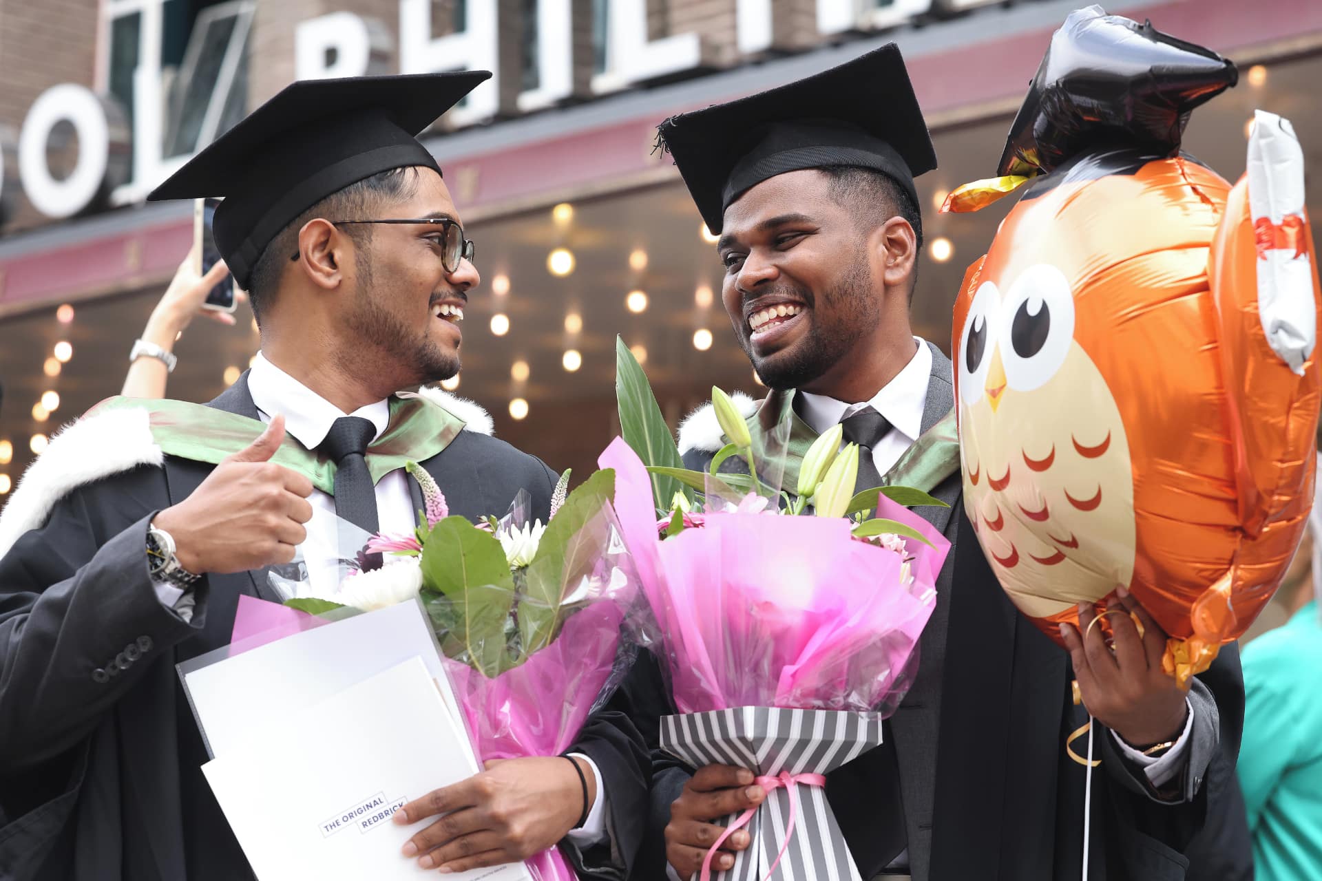 Two students celebrating graduation with balloons and flowers.