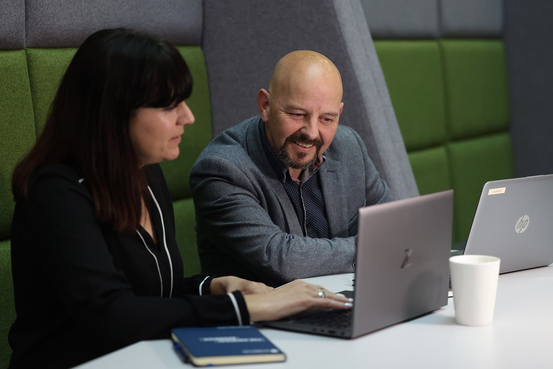 A man and a woman sitting at a table looking at a laptop