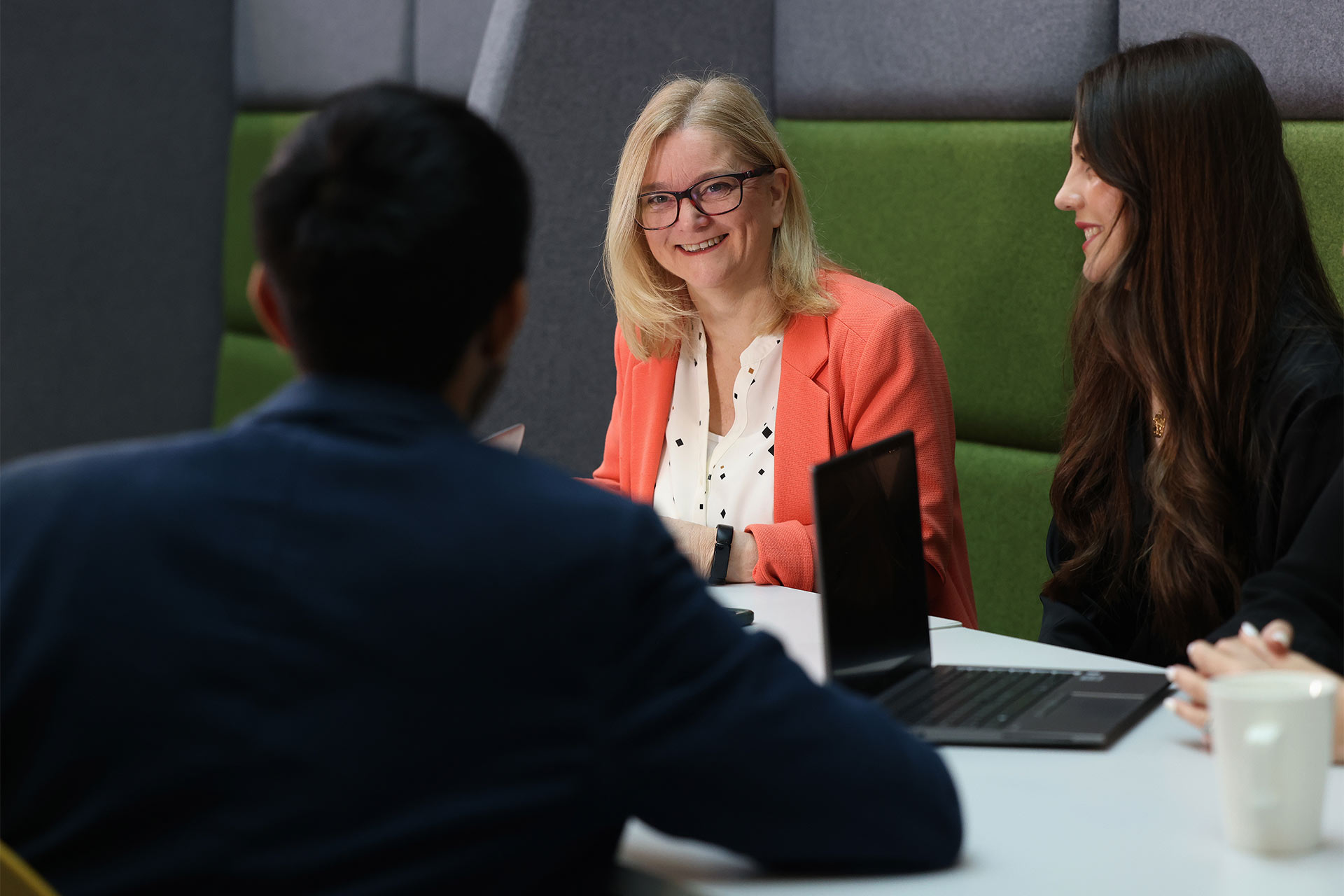 A photograph of staff members at the University of Liverpool sitting around a desk with their laptops and interacting with each other
