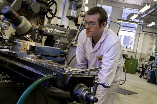 A man in a white lab coat and glasses uses a large piece of equipment in a laboratory setting.