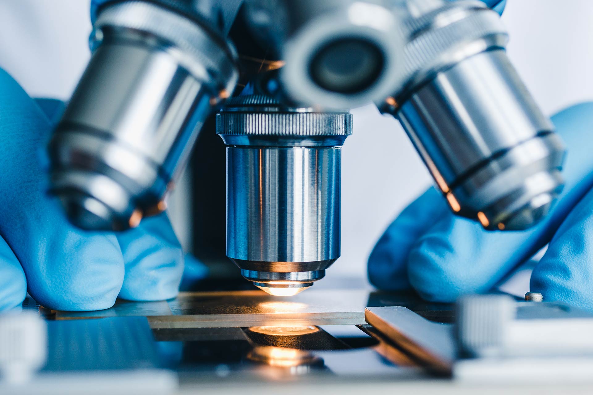 Close-up stock photograph of a researcher working at a microscope. You can see hands holding a sample under the lens.