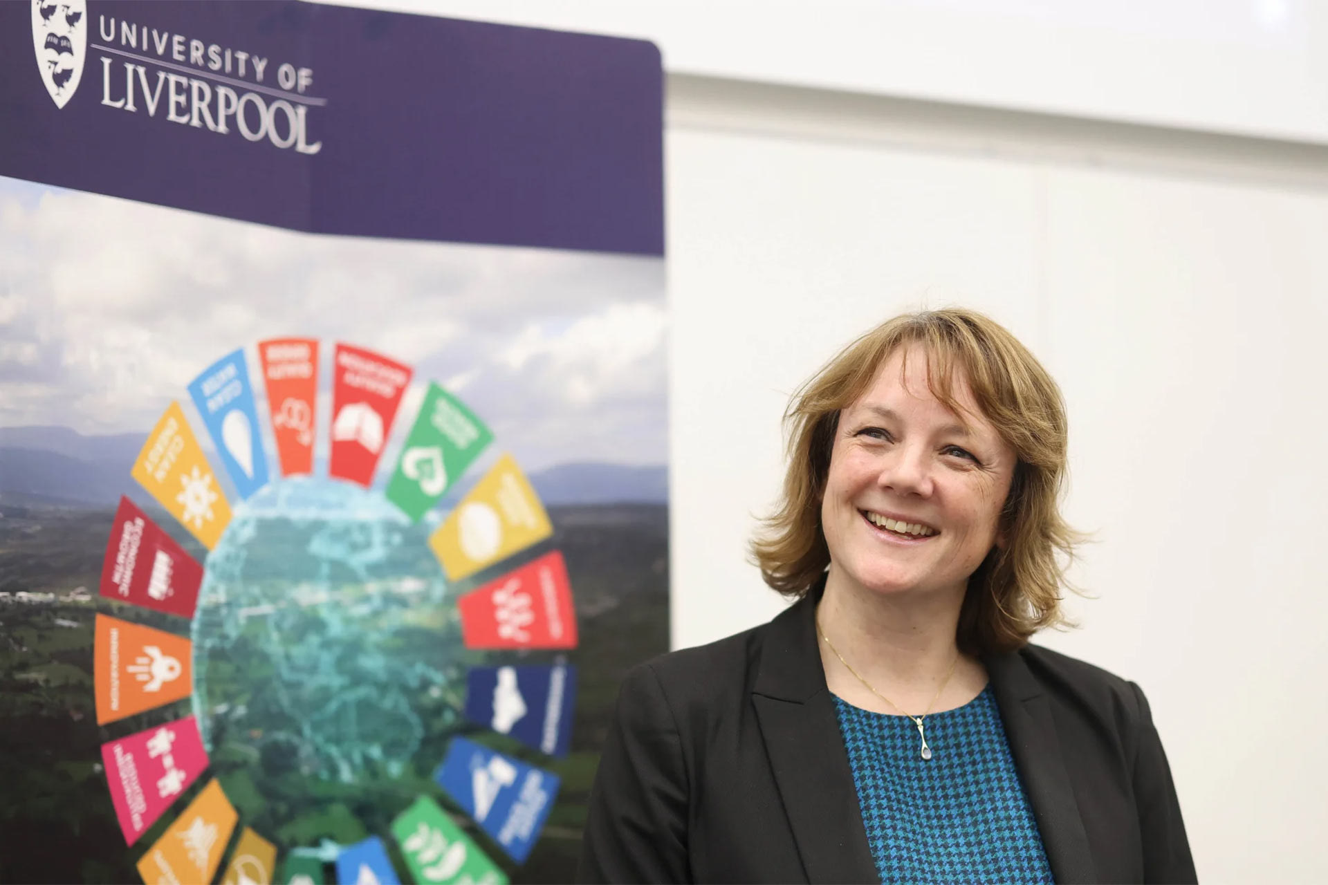 Professor Katie Atkinson stands smiling in front of a display for the University of Liverpool's Interdisciplinary Centre for Sustainability Research