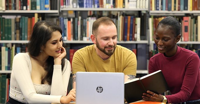 Postgraduate students sitting at a table looking at a notebook and laptop