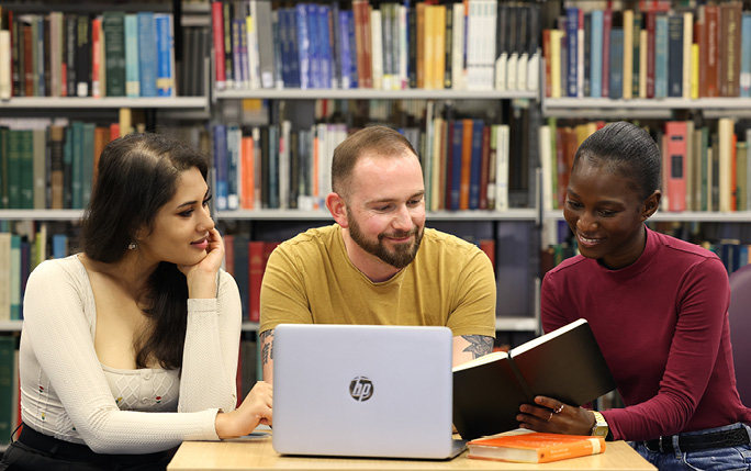 3 postgraduate students sitting at a table looking at a laptop together