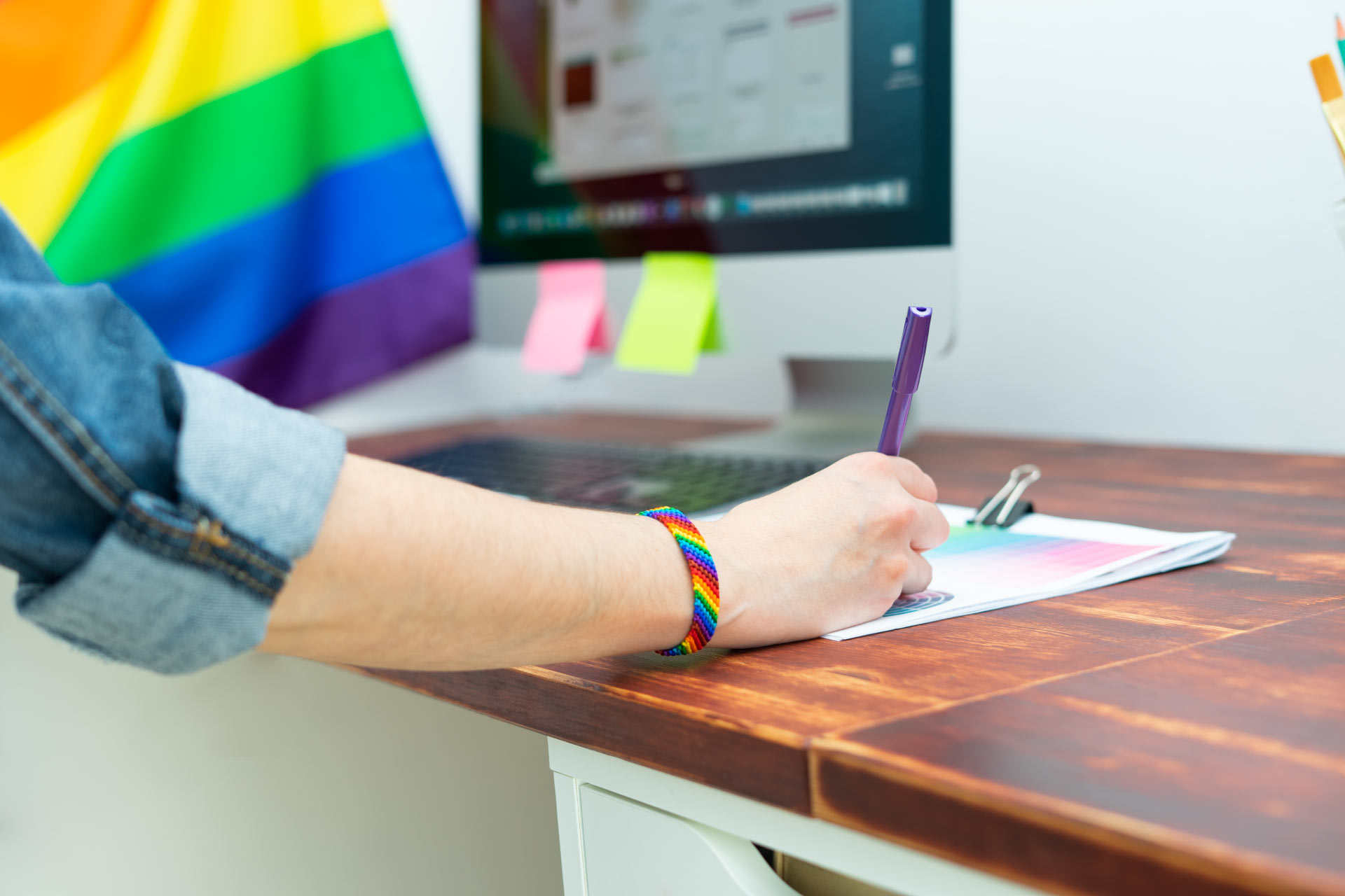 Person writing wears a LGTBIQA+ brazalet