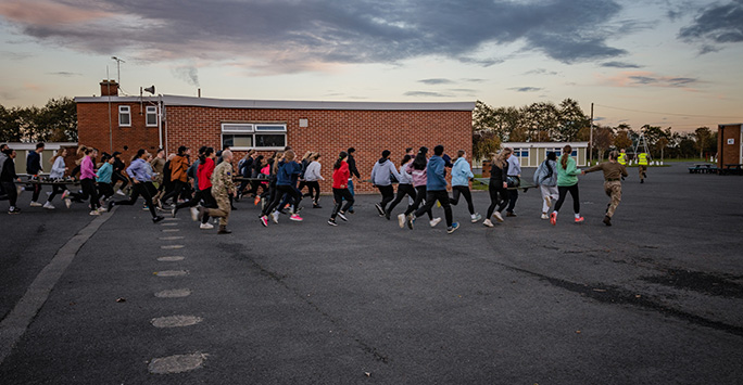 Students running the stretcher relay race through an empty grounds square