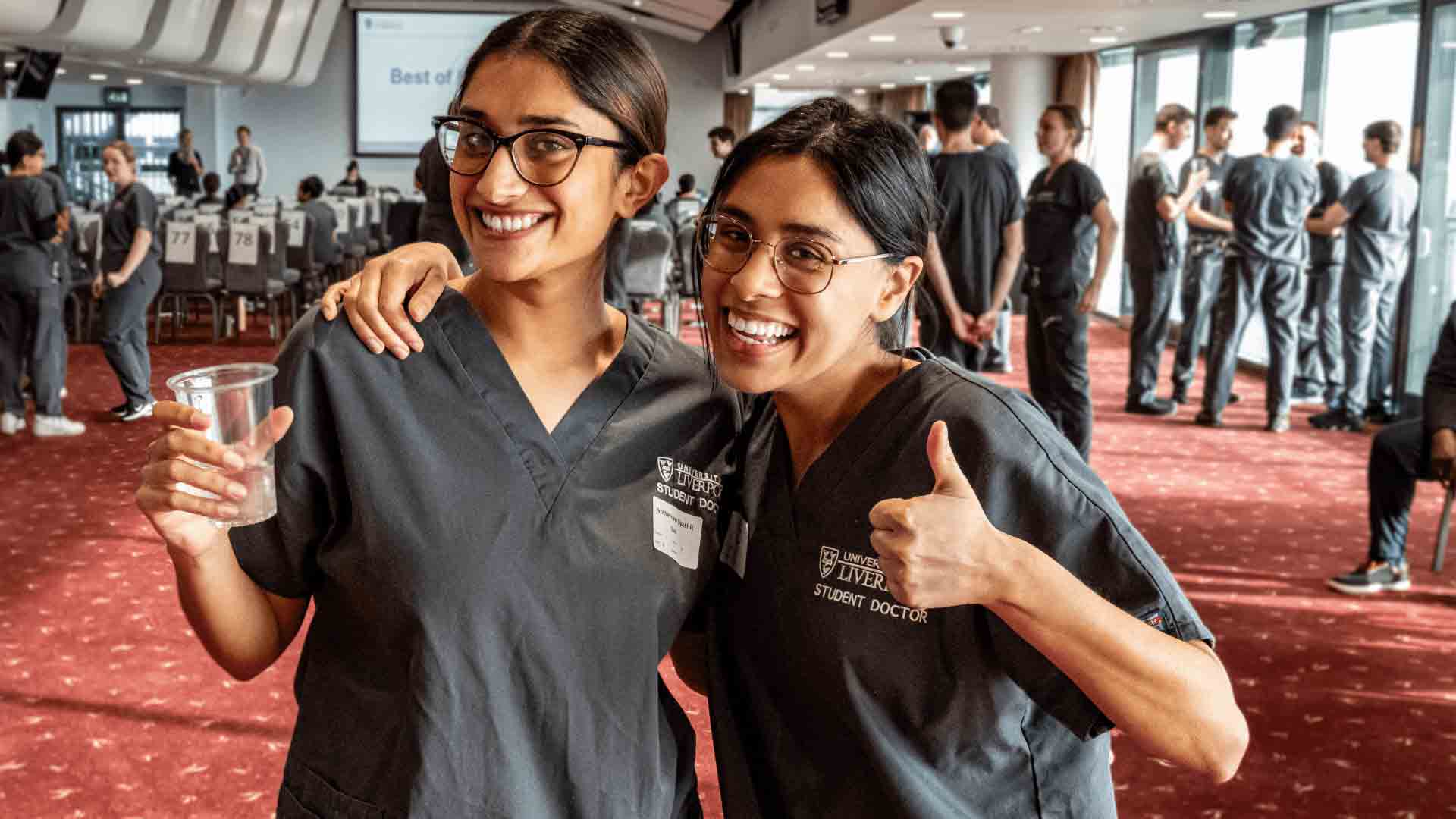 student doctors in grey scrubs give the thumbs up at a clinical assessment